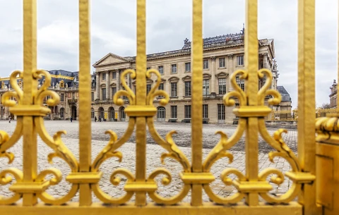 Cour pavée d'un château français historique vue à travers une grille dorée ornementale