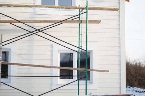 Chantier de construction résidentielle en cours, façade de maison avec échafaudage vert, ouvriers absents, environnement extérieur hivernal avec neige