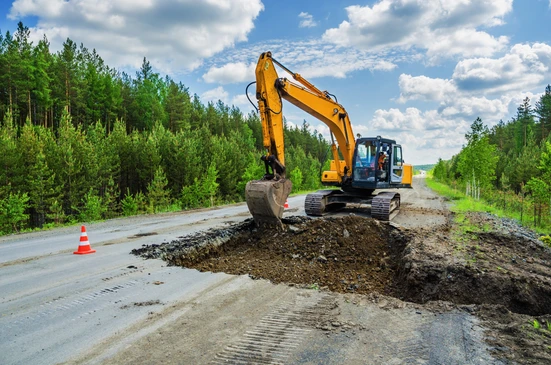 Chantier de construction routière en milieu forestier avec pelleteuse hydraulique sur chenilles effectuant des travaux d'excavation