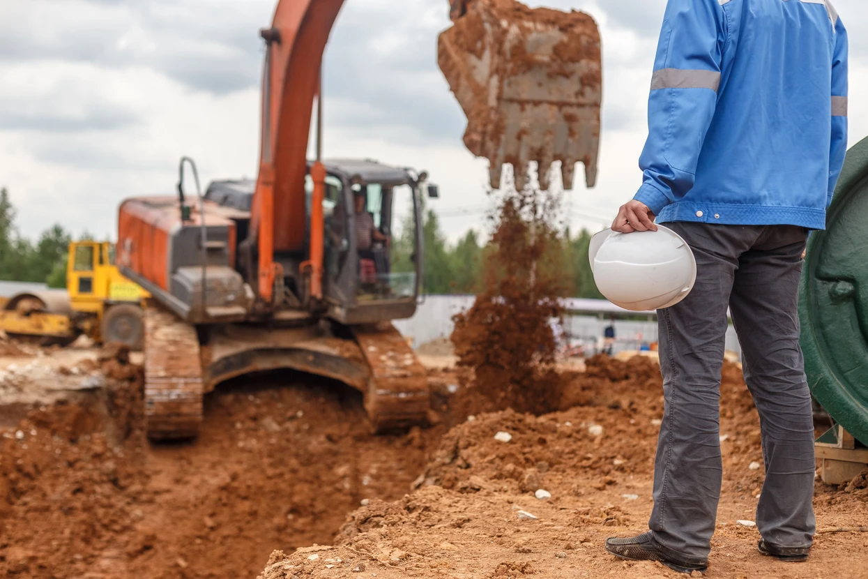 Chantier de construction en extérieur avec ouvrier en vêtements de travail bleus tenant un casque de sécurité blanc
