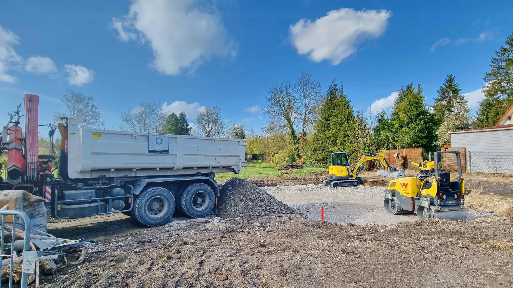 Chantier ext&eacute;rieur avec op&eacute;rateur conduisant une mini-pelle en activit&eacute; de terrassement pr&egrave;s d'une construction en bois
